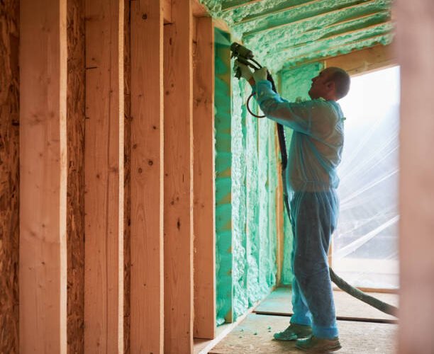 istockphoto-1394617765-612x612 Male builder insulating wooden frame house. Man worker spraying polyurethane foam inside of future cottage, using plural component gun. Construction and insulation concept.