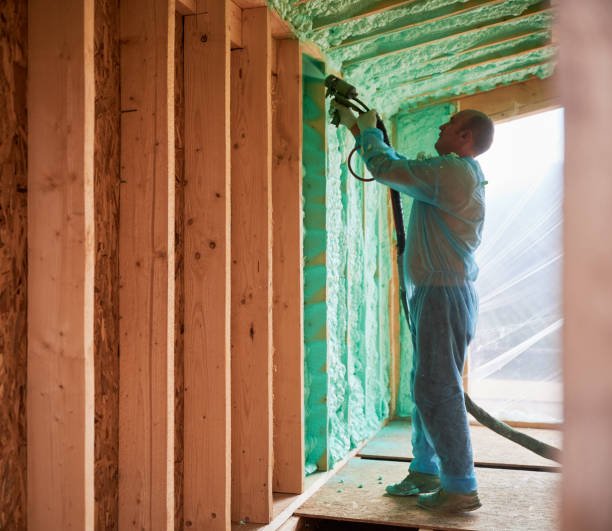 Male builder insulating wooden frame house. Man worker spraying polyurethane foam inside of future cottage, using plural component gun. Construction and insulation concept.